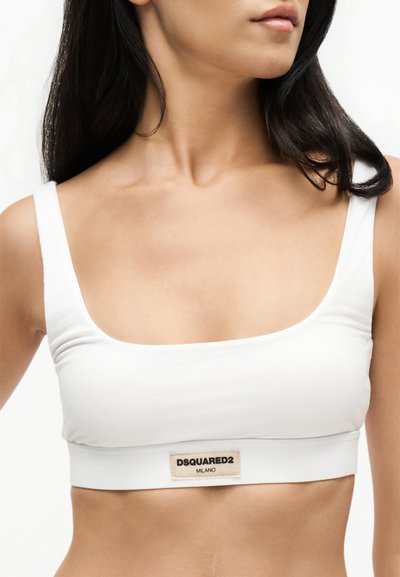 Femme portant un crop top blanc à larges bretelles avec une étiquette DSQUARED2 Milano au centre devant.