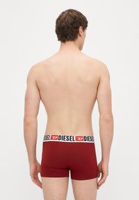 Červené boxerky s čierno-bielym pásom s logom, ktoré majú priliehavý strih a hladkú textúru, pohľad zozadu.