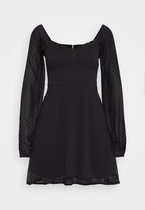 Rochie neagră cu un corp ajustat, mâneci umflate din material transparent cu buline și fustă evazată. Țesătură texturată cu un model subtil și închidere cu fermoar.