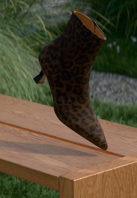 Botín de tobillo con estampado de leopardo y punta afilada, hecho de material suave, con un pequeño tacón apilado y un cierre de cremallera en la parte posterior.
