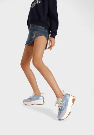 Sneakers azzurri chiari con suole bianche, dotati di chiusura con lacci e dettagli argentati. Il tessuto texturizzato e il design massiccio offrono stabilità.
