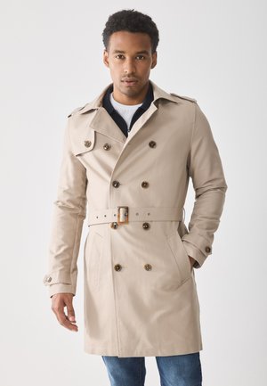 Bež trench coat topelt nööbistamisega ja vööpidi. Omab nurgelise krae ja kahte eesmist taskut. Sile kuma kangas.
