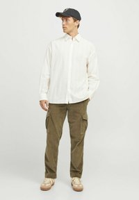 White striped button-up shirt, olive cargo pants with side pockets, beige sneakers, and a black cap with a logo.