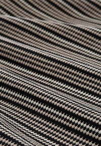 Tissu en tricot avec un motif pied-de-poule en beige, noir et crème. Texture lisse avec un léger étirement, replié en vagues.