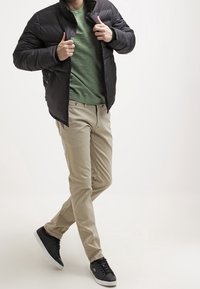 Musta pehmustettu takki, vihreä paita, vaaleat chinot ja mustat urheilukengät. Ominaisuuksiin kuuluvat vetoketjusulku, sivutaskut ja muotoiltu design.