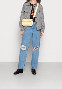 Grå texturerad jacka, svart grafisk t-shirt, ljusblå rivna jeans och svarta ankelstövlar. Gulaxelremsväska med lockstängning.