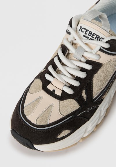 Svarta och beige sneakers med material av mocka och läder, utrustade med vita snören, texturerade detaljer och en dämpad sula.