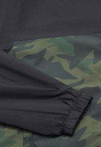Zwarte en groene camouflagejacksectie met elastische manchetten, een gladde textuur en contrasterende stofpanelen.