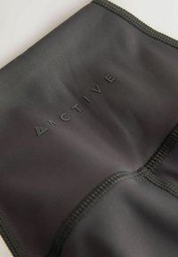 Close-up of black stretch fabric with stitched seams and raised lettering spelling "ACTIVE" in matte black.