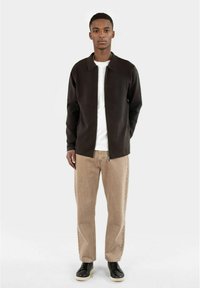 Mörkbrun zip-up jacka över en vit t-shirt, kombinerad med beige raka byxor och svarta skor. Slen tyg, med krage som är synlig.