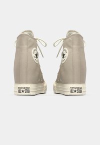 Beige høye sneakers laget av kanvasmateriale, rund tå, hvit gummisåle og klassisk All Star-logo på ankelen. Snøring og øyelet-detaljer.