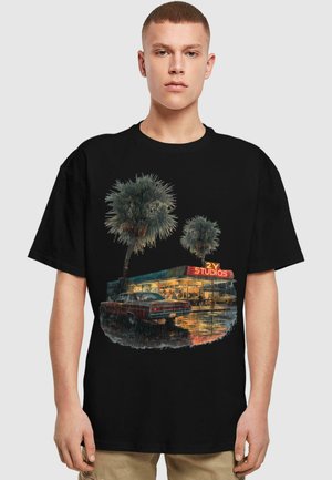 Sort t-shirt med et farverigt grafisk motiv af palmetræer og en vintage bil foran et studio med neonskilt, hvilket skaber en urban scene.
