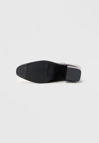 Svart gummisåle av en sko med en glatt overdel og et teksturert grå område ved hælen, med et minimalistisk design.