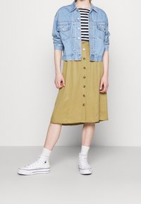 Ljusblå denimjacka över en svart- och vitrandig topp, parat med en khaki midi kjol med knapprad och vita hög-topps sneakers.