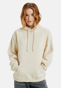 Beige hoodie met trekkoorden, buidelzak en subtiele logo. Gemaakt van zacht materiaal met een ontspannen pasvorm en ribgebreide boorden.