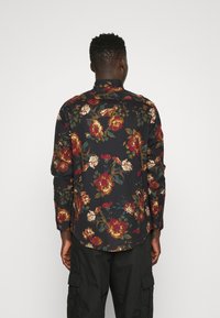 Långärmad skjorta i svart tyg, med ett blommönster i rött, guld och grönt. Rundad nederkant, detaljer med knäppning vid ärmsluten.