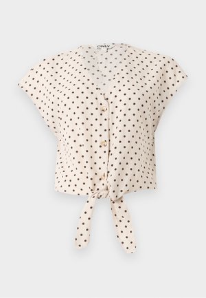 Μπεζ μπλούζα με κοντά μανίκια και μαύρες πουά, κουμπιά στο μπροστινό μέρος, V-λαιμόκοψη και δεμένος κόμπος στη βάση.