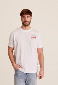 T-shirt en coton blanc avec un graphique coloré sur la poitrine gauche représentant un chef pizzaiolo et le mot "PIZZA". Coupe décontractée avec des manches courtes.