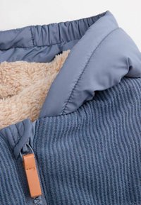 Niebieska kurtka wyściełana polarem, charakteryzująca się teksturą ribbed, gładkim niebieskim materiałem, elastycznym kołnierzem oraz brązowym skórzanym uchwytem zamka.