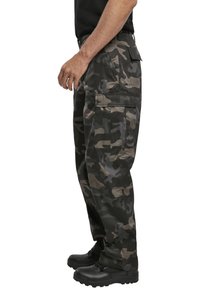 Lastbyxor i camouflage-mönster med mörkgrön, svart och brun färg. Tillverkade av slitstarkt material med flera fickor.