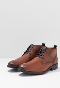 Bottines en cuir marron avec une finition lisse, dotées d'un accent tissé au col et d'une semelle en caoutchouc bleu foncé. Design à lacets.