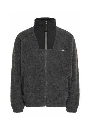 Veste en polaire grise avec col haut et fermeture éclair, ornée de panneaux noirs et de poches latérales. Surface douce et texturée.