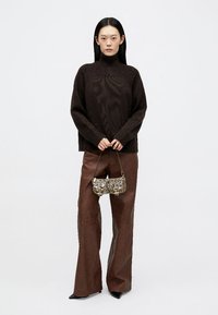 Maglione a collo alto lavorato a maglia marrone abbinato a pantaloni a gamba larga in finta pelle marrone e una borsa metallica con tracolla a catena.