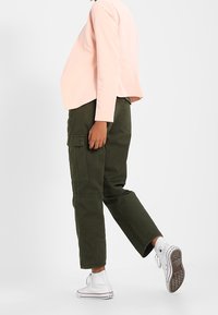 Light pink cropped jacket, olive green cargo pants, and white high-top sneakers. Features include pockets on pants and a smooth texture.