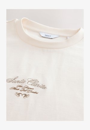 Kremowy t-shirt z prążkowanym dekoltem i brązowym haftowanym napisem „Santa Clarita” oraz ozdobnym akcentem.
