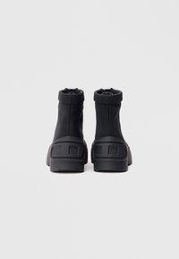 Černé kotníkové boty s hladkým, pružným svrškem, kulatou špičkou a texturovanou gumovou podrážkou. Mají polstrovaný límec a design s širokým podpatkem.