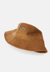 Cappello a secchiello in corduroy marrone con una texture a coste e un logo di coccodrillo verde ricamato sul lato anteriore.