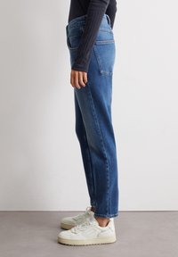 Jeans in denim azzurro chiaro con una vestibilità dritta, caratterizzati da un alto punto vita e tasche posteriori, abbinati a sneakers bianche.