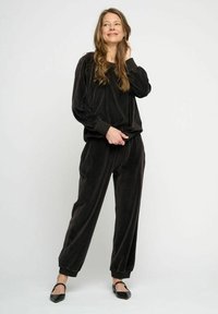 Svart velour loungemodell bestående av en avslappnad långärmad topp och smala byxor med ribbade manschetter, i kombination med svarta lägenheter.