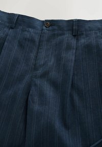 Pantalon bleu foncé avec fines rayures blanches verticales, fermeture à boutons et passants pour ceinture à la taille.