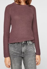 Sweter dzianinowy w głębokim odcieniu mauve, z prążkowaną fakturą, okrągłym dekoltem i długimi rękawami, zestawiony z szarymi dżinsami.
