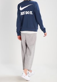 Marinblå sweatshirt med texten "JUST DO IT." i vitt, gråa sweatpants och vita sneakers. Avslappnad passform och mjukt tyg.
