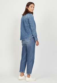 Denim shirt and pants set in light blue, featuring a relaxed fit. The shirt has long sleeves with button cuffs; pants are ankle-length. White sneakers.