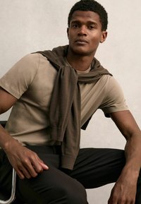 Bēša īsroku t-krekls, pievienots ar tumši brūnu džemperi, kas sasiets ap pleciem, valkāts ar melnām biksēm. Gluda auduma, ikdienišķa piegriezuma.