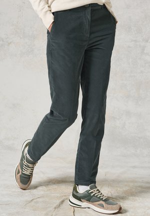Tmavě zelené manšestrové kalhoty s hladkou texturou, rovného střihu a bočními kapsami, spárované se zeleno-beige sportovními teniskami.