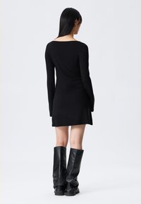 Czarna, dopasowana sukienka z długimi rękawami i kwadratowym dekoltem, z marszczeniem z tyłu. Noszona z czarnymi kozakami za kolano.