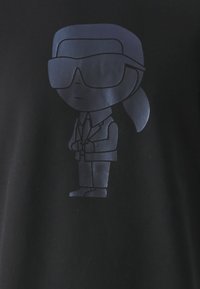 T-shirt nera con una grafica di una figura stilizzata che indossa occhiali da sole, un completo e tiene le mani, con una finitura liscia e opaca.