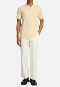 Polo en jaune pâle, à manches courtes, en tissu doux. Associe à un pantalon blanc et des chaussures noires à semelles texturées.