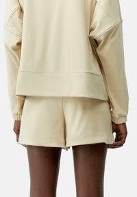Suéter beige con hombros caídos y shorts a juego. Tela suave y lisa con puños y dobladillo elásticos. Diseño minimalista, sin patrones ni acentos.