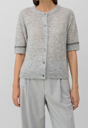 Femme portant un cardigan en maille gris clair à manches courtes avec des boutons et un pantalon ample gris clair assorti.