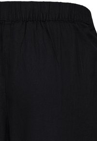 Ceinture élastique noire sur tissu texturé, avec de fines fronces et une couture simple visible sur le côté gauche.