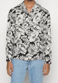 Zwarte longsleeve met een witte bloemenprint en ingewikkelde details. Dit shirt heeft een losse fit en een geknipte kraag.