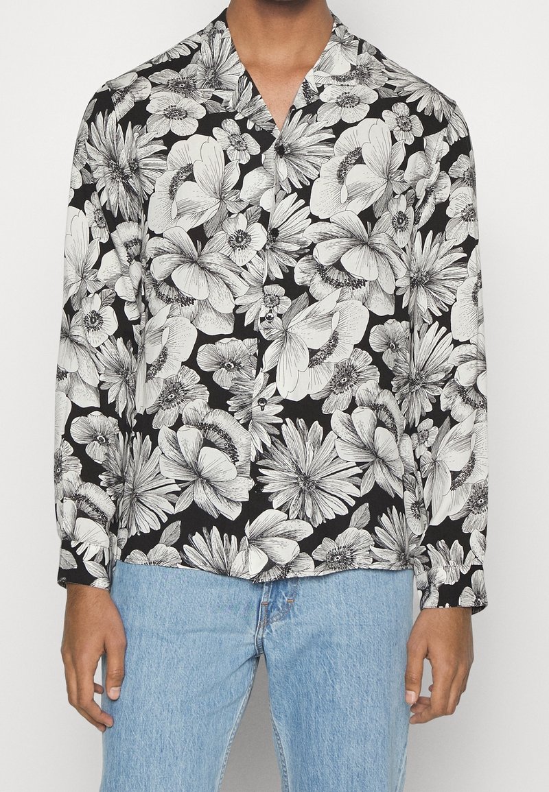 Zwarte longsleeve met een witte bloemenprint en ingewikkelde details. Dit shirt heeft een losse fit en een geknipte kraag.