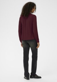 Bordeaux langærmet skjorte med krave, parret med sorte jeans og sorte loafers. Krøllet hår, vendt let til siden. Enkel design.