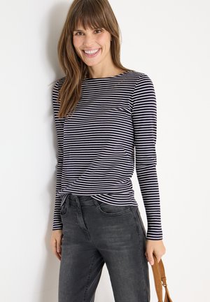 Marineblauw en witte gestreepte langemouwen top met een ronde hals, geknoopt detail bij de taille, gecombineerd met donkergrijze jeans en een lichtbruine tas.