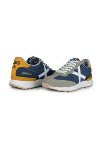 Zapatillas en azul marino y gris con un diseño de ante y malla. Presentan detalles en blanco, talón amarillo y una suela texturizada. Incluyen cordones y logo.